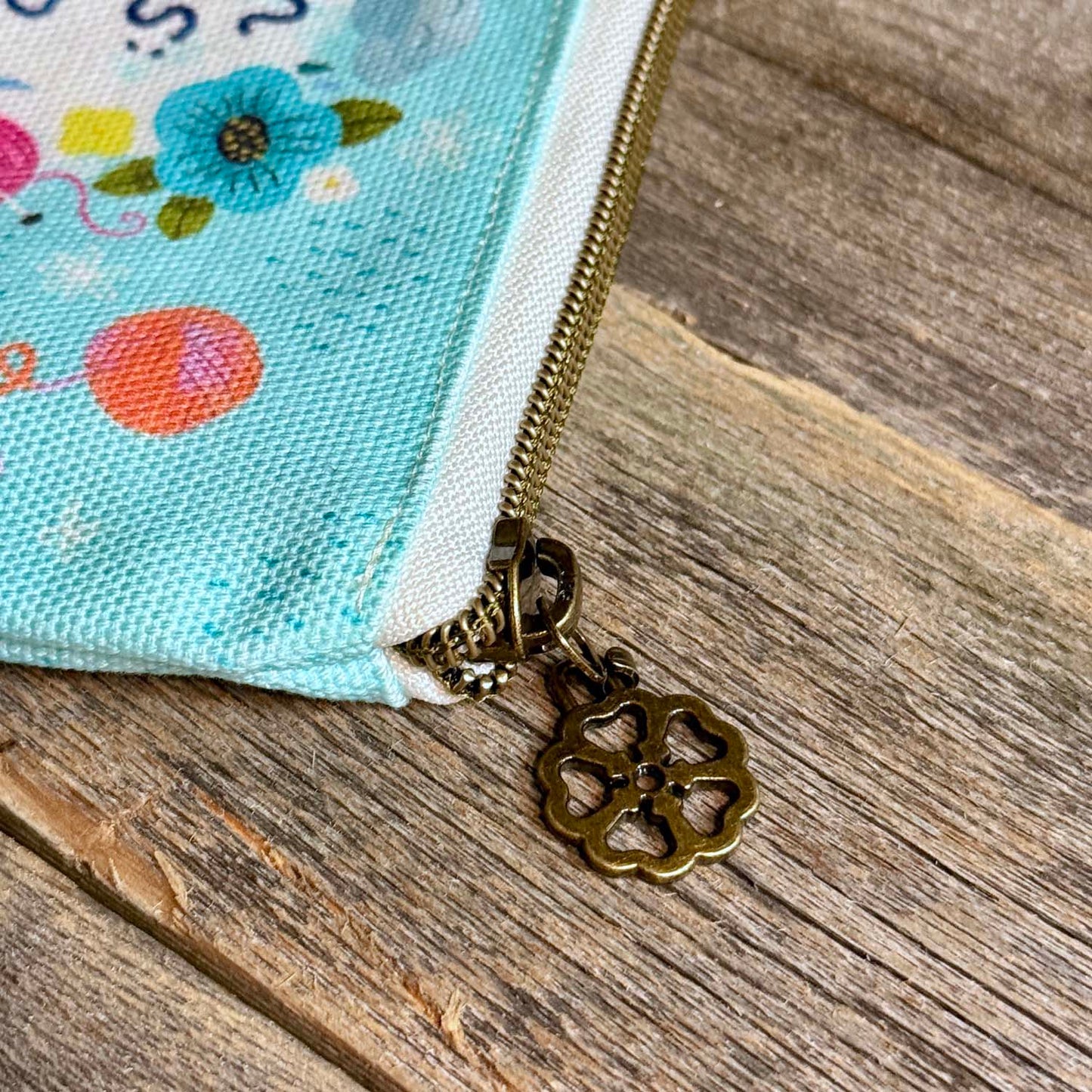 blue green canvas zippered pouch printed with yarn and flowers that says "rain rules drop everything and knit"