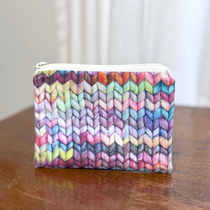 Colorful knitted patterned pouch on a wooden surface with a blurred white background