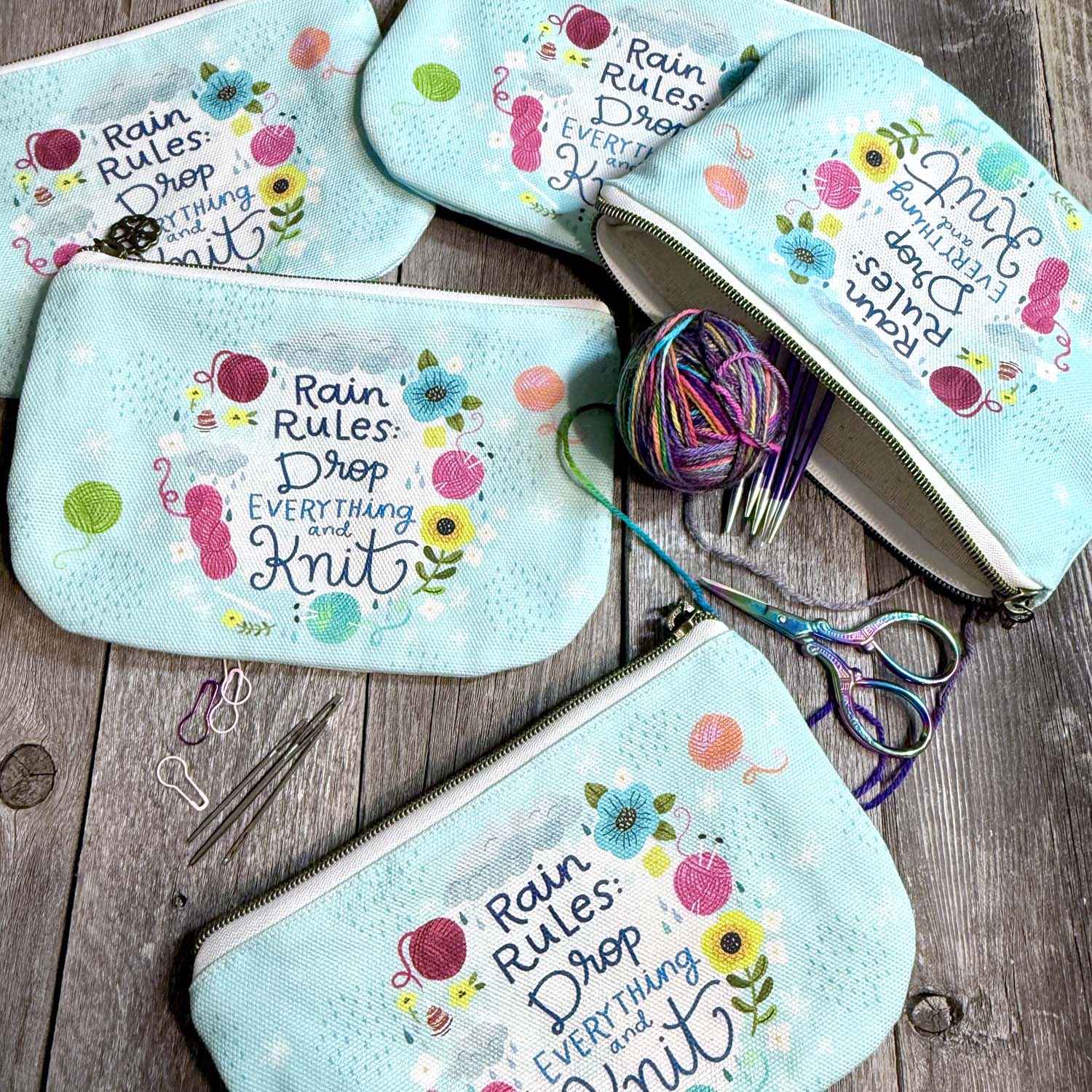 blue green canvas zippered pouch printed with yarn and flowers that says "rain rules drop everything and knit" 