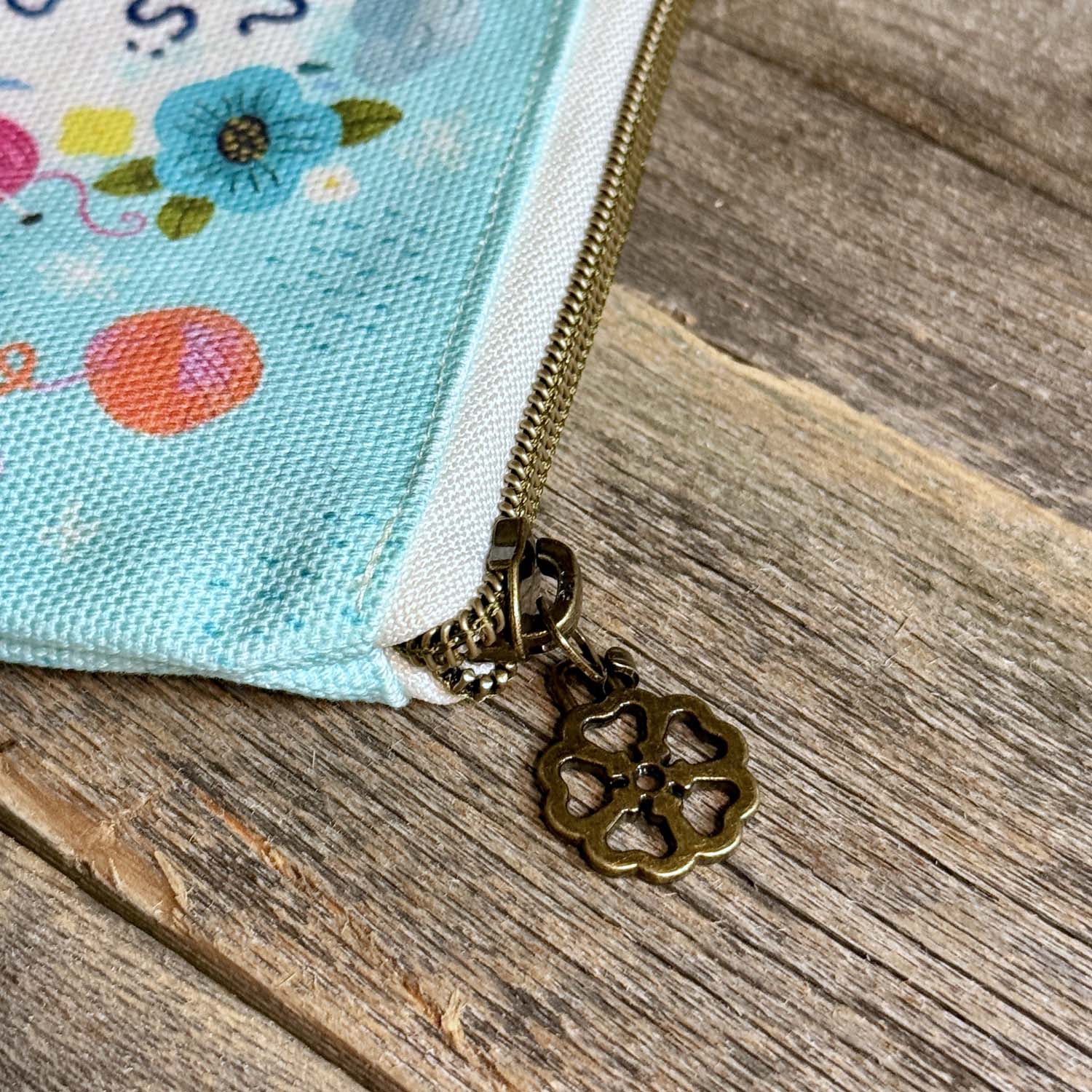 blue green canvas zippered pouch printed with yarn and flowers that says "rain rules drop everything and knit" 