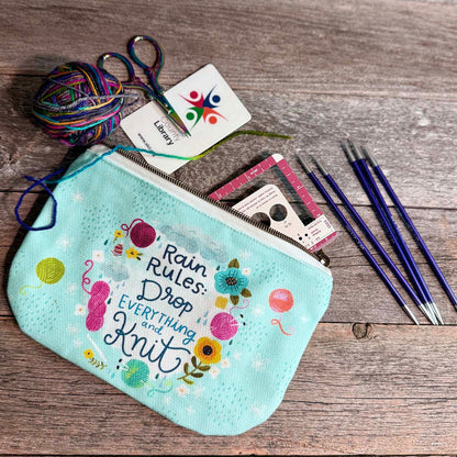 blue green canvas zippered pouch printed with yarn and flowers that says "rain rules drop everything and knit" 