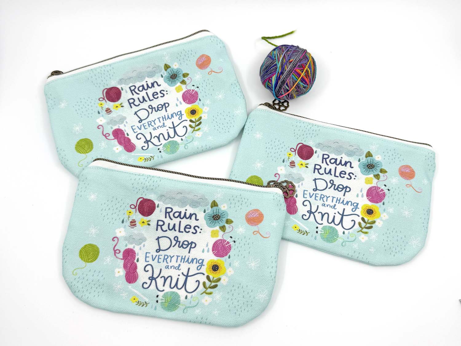 blue green canvas zippered pouch printed with yarn and flowers that says "rain rules drop everything and knit" 