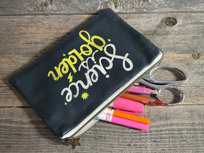 Black pouch with colorful text and pens on a wooden surface