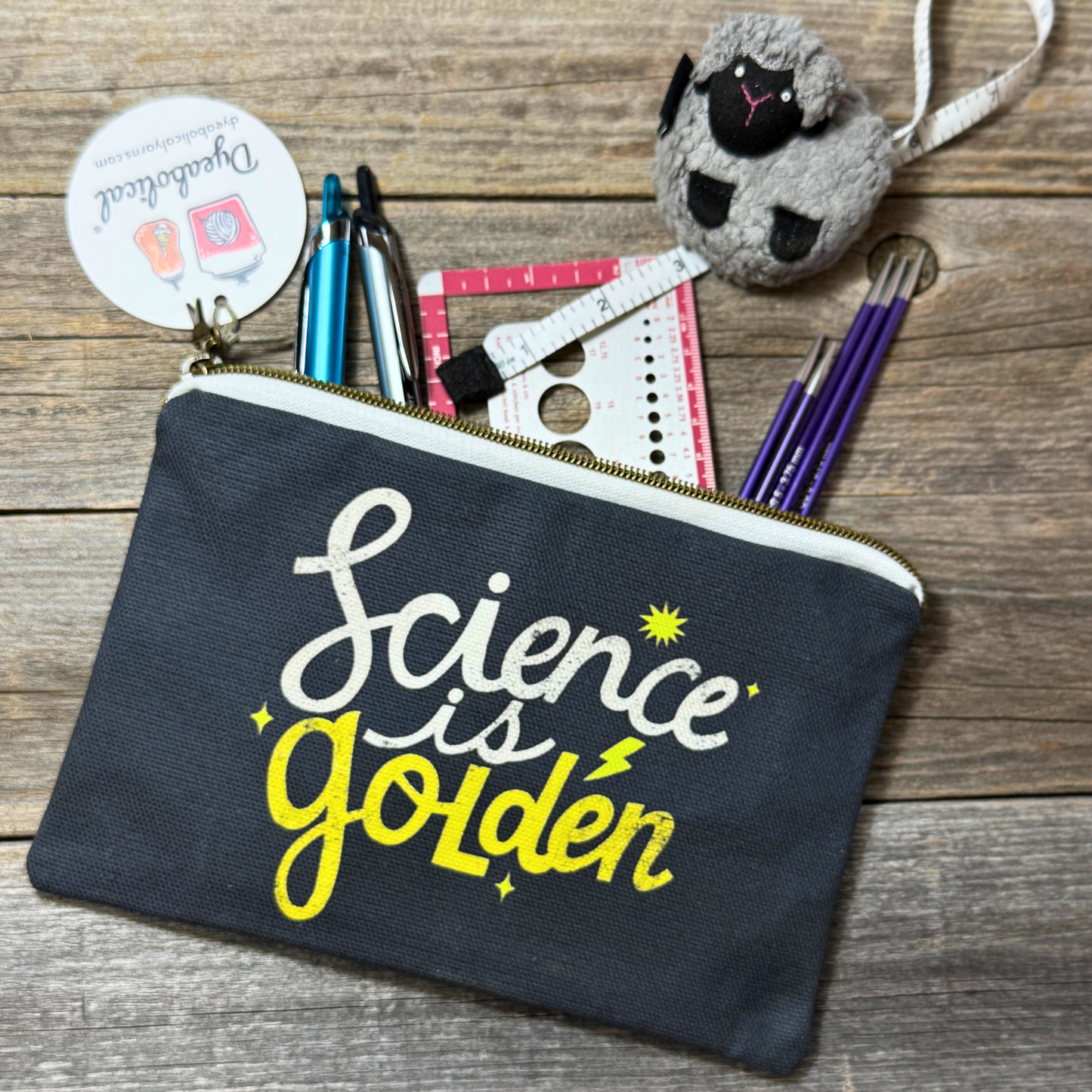 Black pouch with 'Science is Golden' text on a wooden surface with stationery items.